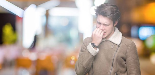 Jonge knappe man dragen winterjas over geïsoleerde achtergrond op zoek gestresst en nerveus met handen op mond nagels te bijten. Angst probleem. - Foto, afbeelding