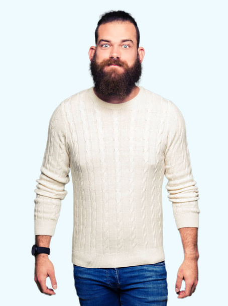 Νέοι hipster άνθρωπος φορώντας χειμώνα πουλόβερ ξεφυσώντας μάγουλα με αστείο πρόσωπο. Στόμα άσκησης φουσκώνουν με αέρα, τρελό έκφραση. - Φωτογραφία, εικόνα