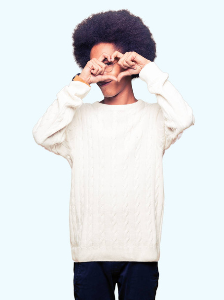 Jeune homme afro-américain aux cheveux afro portant des lunettes Faire forme de coeur avec la main et les doigts souriant en regardant à travers signe
 - Photo, image