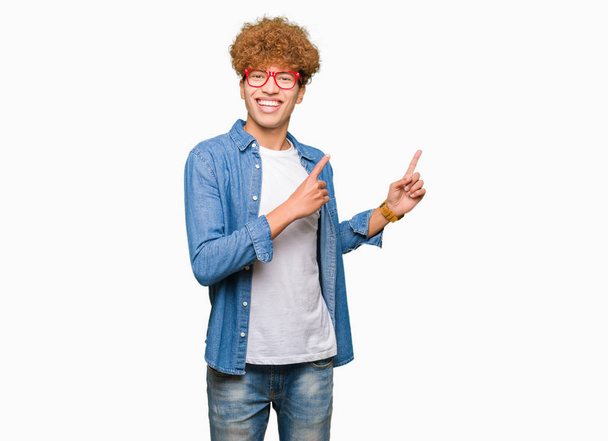 Young handsome man with afro hair wearing glasses smiling and looking at the camera pointing with two hands and fingers to the side. - Photo, image