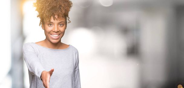 Mooie jonge Afro-Amerikaanse vrouw op geïsoleerde achtergrond lachende vriendelijke aanbod als begroeting en het welkom heten handdruk. Succesvol bedrijf. - Foto, afbeelding