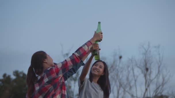 Group of a young teen Asian woman celebrates with friends camping in nature having fun together drinking beer and clinking glasses. Drinking beer and looking view while sunset with friends. - Materiał filmowy, wideo