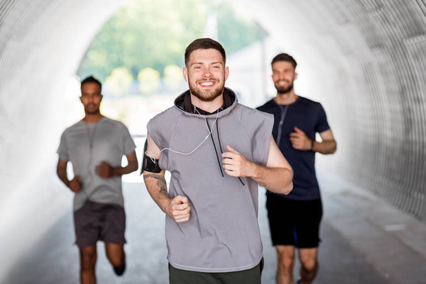 male friends with earphones running outdoors - Photo, image