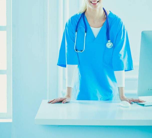 Junge Ärztin steht am Tisch, isoliert auf weißem Hintergrund - Foto, Bild