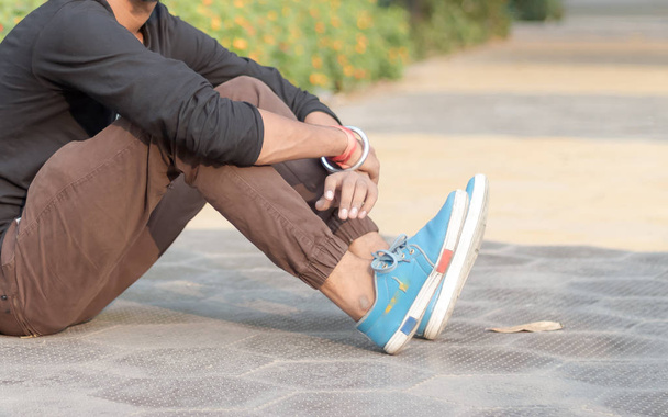 Close up Cropped image of young sportsman, athlete man in sports clothing sitting on track and field near playground and relaxing after jogging or warm up exercise at morning time of day. Front view.  - Foto, Imagem
