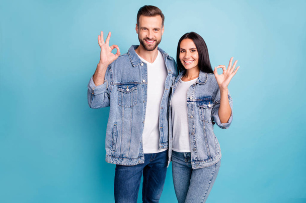 Portrait of charming couple making okay sign wearing denim jeans isolated over blue background - Valokuva, kuva