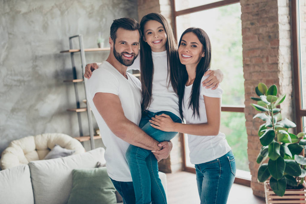 Portrait of nice attractive lovely affectionate sweet careful cheerful family wearing casual white t-shirts jeans carrying pre-teen brunette schoolgirl at industrial loft style interior living-room - Foto, Bild