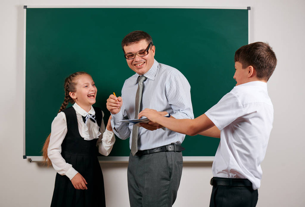 Portrait of a teacher checking homework, reading school exercise books, schoolboy and schoolgirl with old fashioned eyeglasses posing on blackboard background - back to school and education concept - Photo, Image