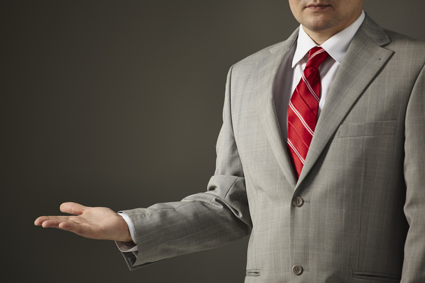 επιχειρηματίας με ένα γκρι κοστούμι δείχνει ένα άδειο χέρι - Φωτογραφία, εικόνα