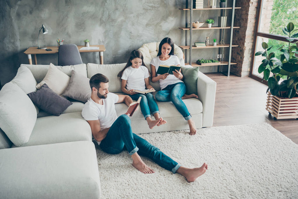 Nice attractive lovely charming friendly focused cheerful cheery idyllic family wearing casual white t-shirts jeans reading book hobby at industrial loft style interior living-room indoor - Fotoğraf, Görsel