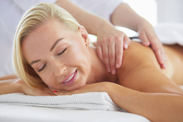Young woman in spa salon, getting stones massage - Foto, imagen