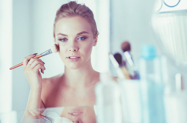 A picture of a young woman applying face powder in the bathroom - Foto, afbeelding