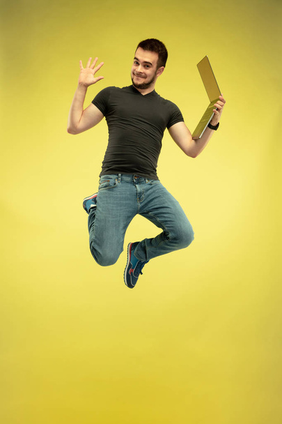 Full length portrait of happy jumping man with gadgets on yellow background - Фото, зображення