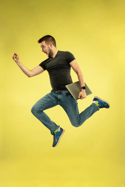 Full length portrait of happy jumping man with gadgets on yellow background - Valokuva, kuva