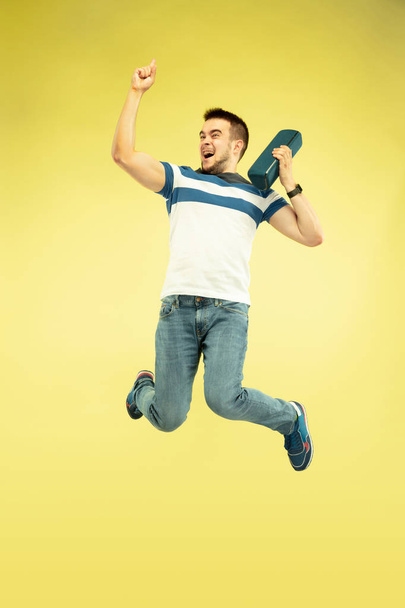 Full length portrait of happy jumping man with gadgets on yellow background - Foto, Bild