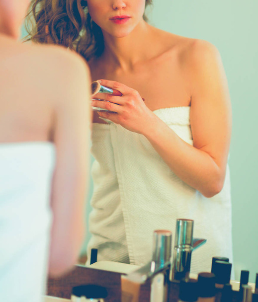 Молода жінка дивиться у дзеркало і одягає макіяж
. - Фото, зображення