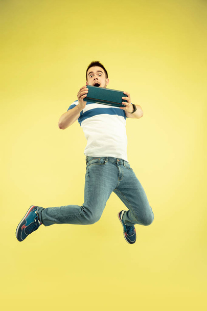 Full length portrait of happy jumping man with gadgets on yellow background - 写真・画像