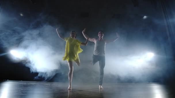 um par de dançarinos no palco em fumaça e holofotes se movendo rápido
 - Filmagem, Vídeo