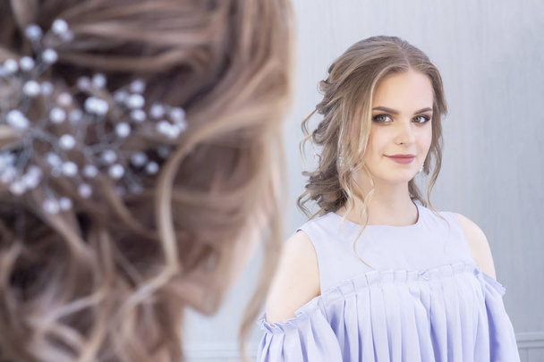 beautiful girl with a wedding hairstyle looks at herself in the mirror, portrait of a young girl. beautiful make-up. beauty saloon - Foto, Bild