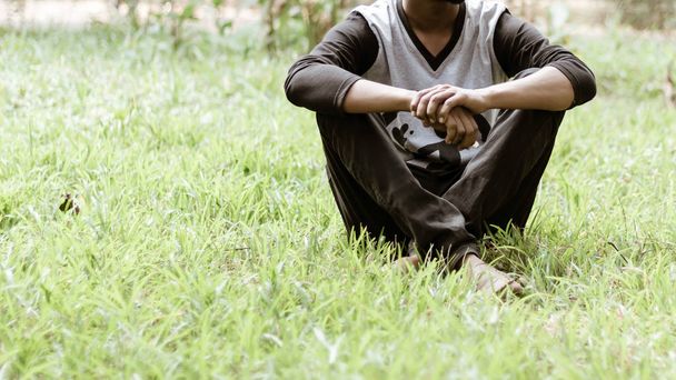 Close up Cropped image of young man in casual clothing sitting over green grass in the park at morning time of day. Front view. Concept of spending leisure time in open air surrounded by nature. The h - Photo, Image
