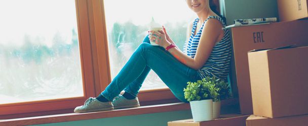 Girl sitting on windowsill at new home with cup - 写真・画像