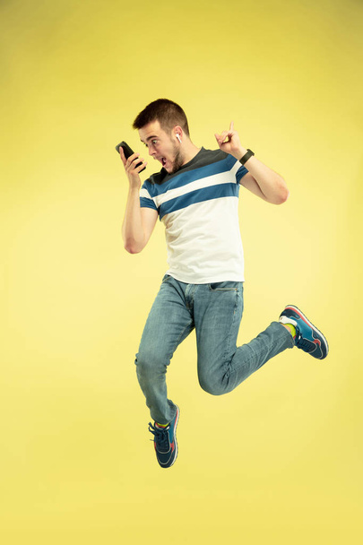 Full length portrait of happy jumping man with gadgets on yellow background - Fotó, kép