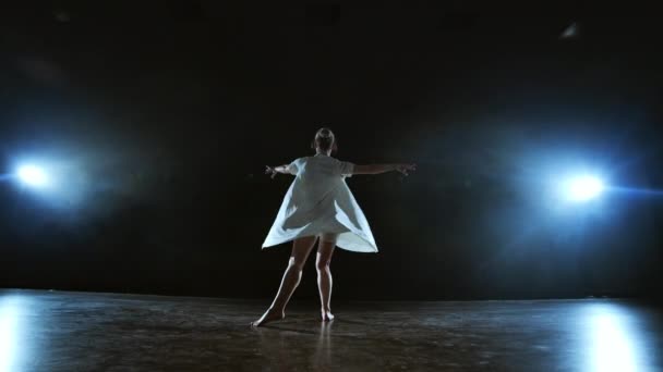 dziewczynka w białej sukni tańczy współczesnych obrotów na scenie z dymem w reflektorach. - Materiał filmowy, wideo