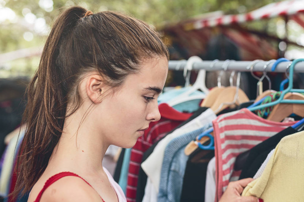 νεαρή γυναίκα περιήγηση ρούχα σε μια υπαίθρια αγορά - Φωτογραφία, εικόνα