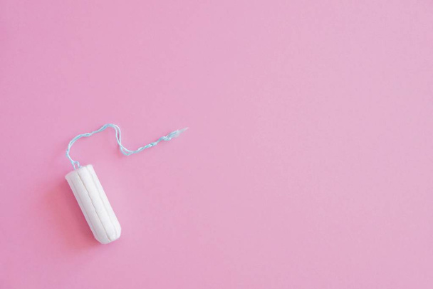 One hygienic tampon on a pink background. Menstrual mothly cycle, means of protection. Top view, flat lay, copy space for text. - Foto, Imagen