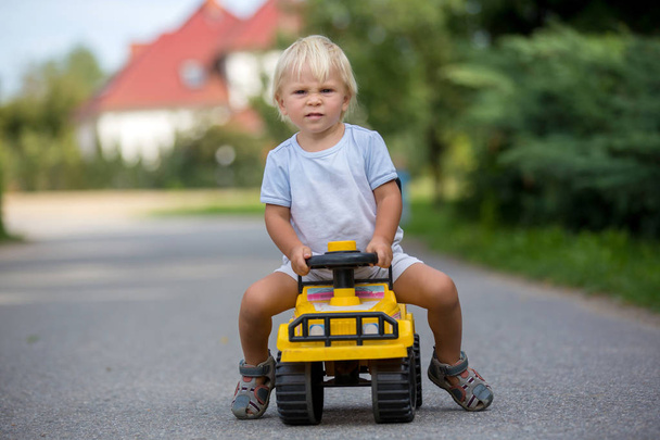 Sweet toddler boy, riding plastic toycar on the street in quiet  - 写真・画像