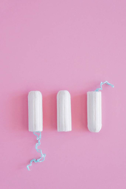 Three hygienic tampons on a pink background. Menstrual mothly cycle, means of protection. Top view, flat lay, copy space for text. - Zdjęcie, obraz