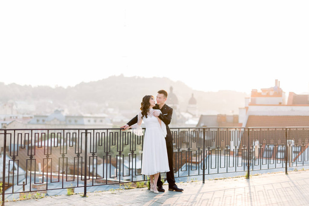 Chinese groom handsome man and pretty bride young cute woman in white wedding dress, asian couple standing outdoors on city terrace, panoramic view of old city - Photo, Image