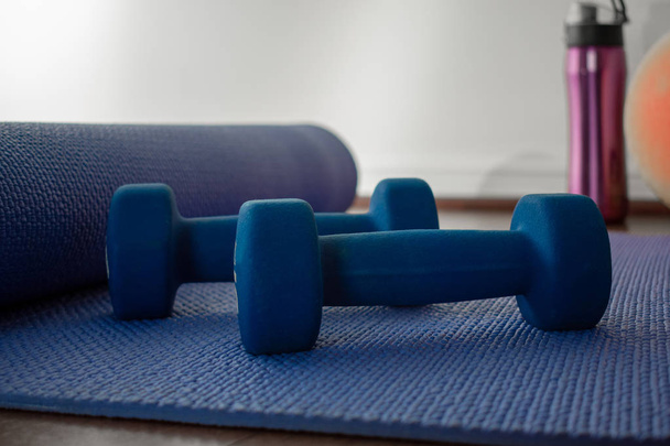 Esterilla de yoga azul con mancuernas y botella de agua en el suelo del gimnasio
  - Foto, Imagen