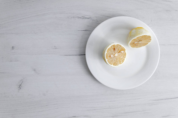 Μισό λεμόνι σε λευκό πιάτο στο φόντο ενός γκρι ξύλινου τραπεζιού. - Φωτογραφία, εικόνα