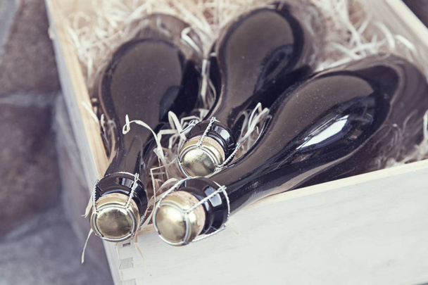 bir taş duvar arka plan üzerinde ahşap bir kutu içinde üç şampanya şişeleri - Fotoğraf, Görsel