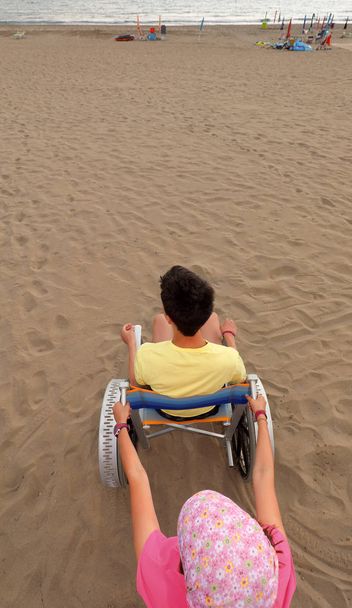 小さな女の子は、あなたがと砂浜に車椅子をプッシュ - 写真・画像