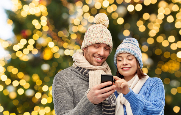 happy couple with smartphone over christmas lights - Foto, imagen