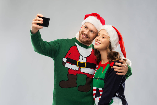 happy couple in christmas sweaters taking selfie - 写真・画像