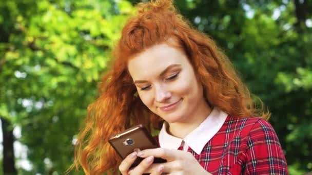 Red haired girl typing message on phone outside - Filmati, video