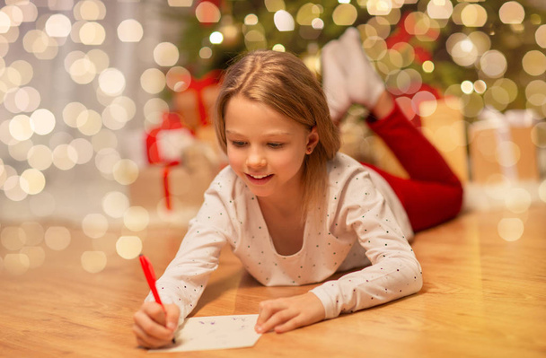 smiling girl writing christmas wish list at home - 写真・画像