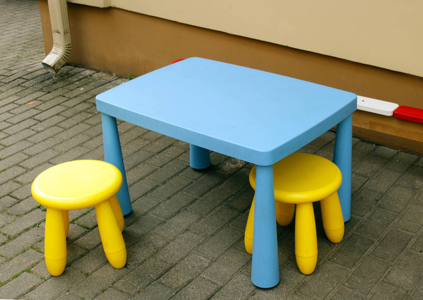 Dziecięce meble ogrodowe niebieski stół i żółte krzesła na chodniku kaflowy - Zdjęcie, obraz