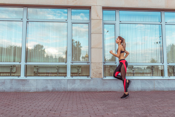 sports girl in summer city, runs morning run, background glass windows of business building, burning calories, cardio fitness training day and morning. Healthy lifestyle style. Free space for text. - Valokuva, kuva