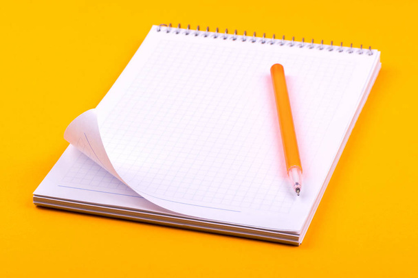 黄色のペンの横に、図面、テキスト、ノート用の白い紙の紙が付いた春のノートブックは、オレンジ色の背景に横たわっています - 写真・画像