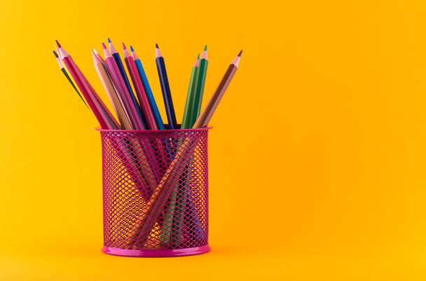 Lápices afilados de madera de colores para dibujar en un soporte redondo de frambuesa sobre un fondo cercado
 - Foto, imagen