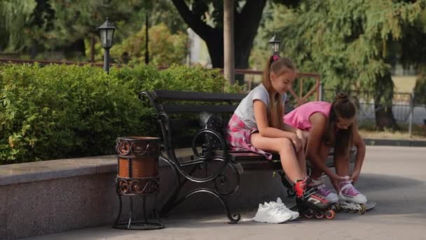 Teen girls sitting on a bench puts on roller skates - Footage, Video
