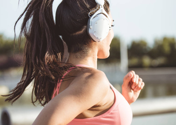 Brown and attractive Venezuelan woman, goes running with big headphones to listen music - Photo, Image
