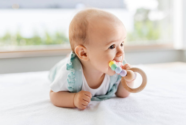 baby girl on white blanket chewing wooden rattle - Photo, Image