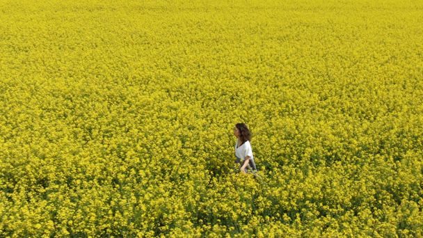 όμορφη μελαχρινή περπατάει κατά μήκος ατέλειωτο κίτρινο λουλούδι πεδίο - Φωτογραφία, εικόνα