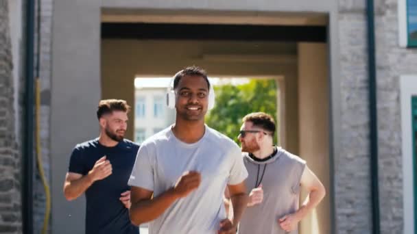 male friends with headphones running outdoors - Imágenes, Vídeo