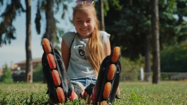 Nuori tyttö istuu nurmikolla ihaillen rullaluistimet
 - Materiaali, video